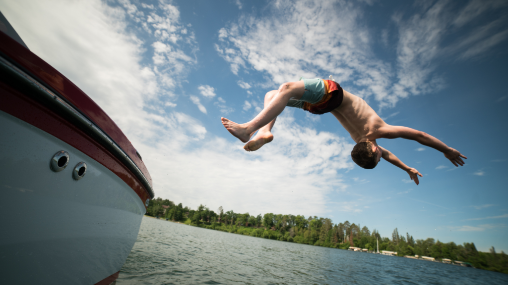 Child doing a backflip off of a bat into the water.