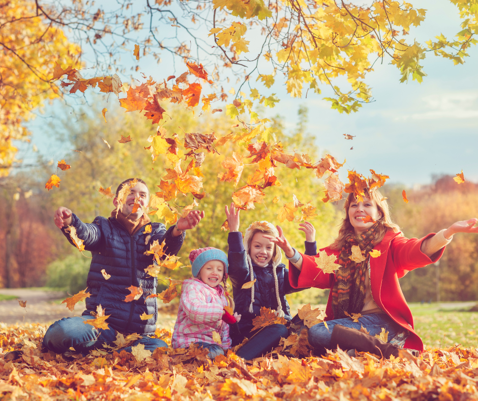 family throwing leaves in the air while sitting on ground
